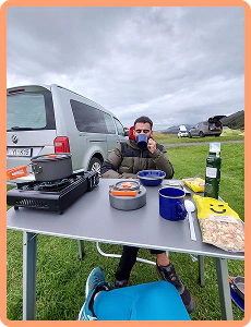 Cliente che fa colazione a un tavolo da campeggio accanto al suo Caddy Beach in Islanda